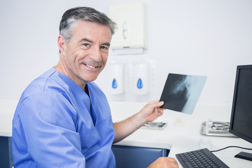 Zahnarzt hält Röntgenbild und schaut in die Kamera
